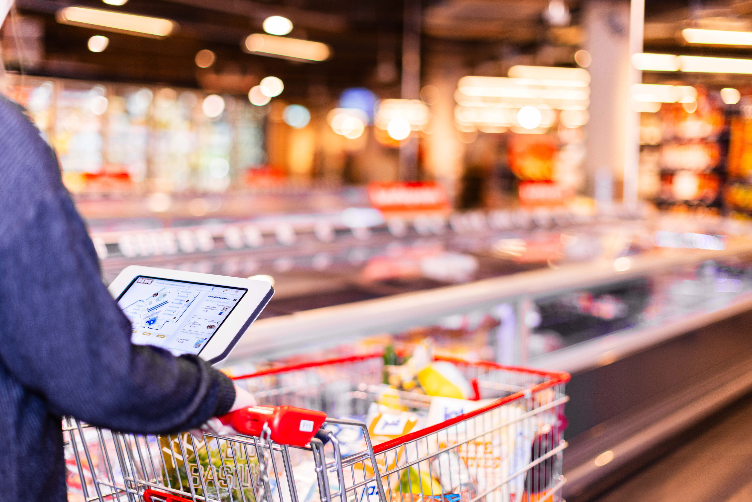 Einkaufswagen mit REWE Catch auf dem Display im Markt