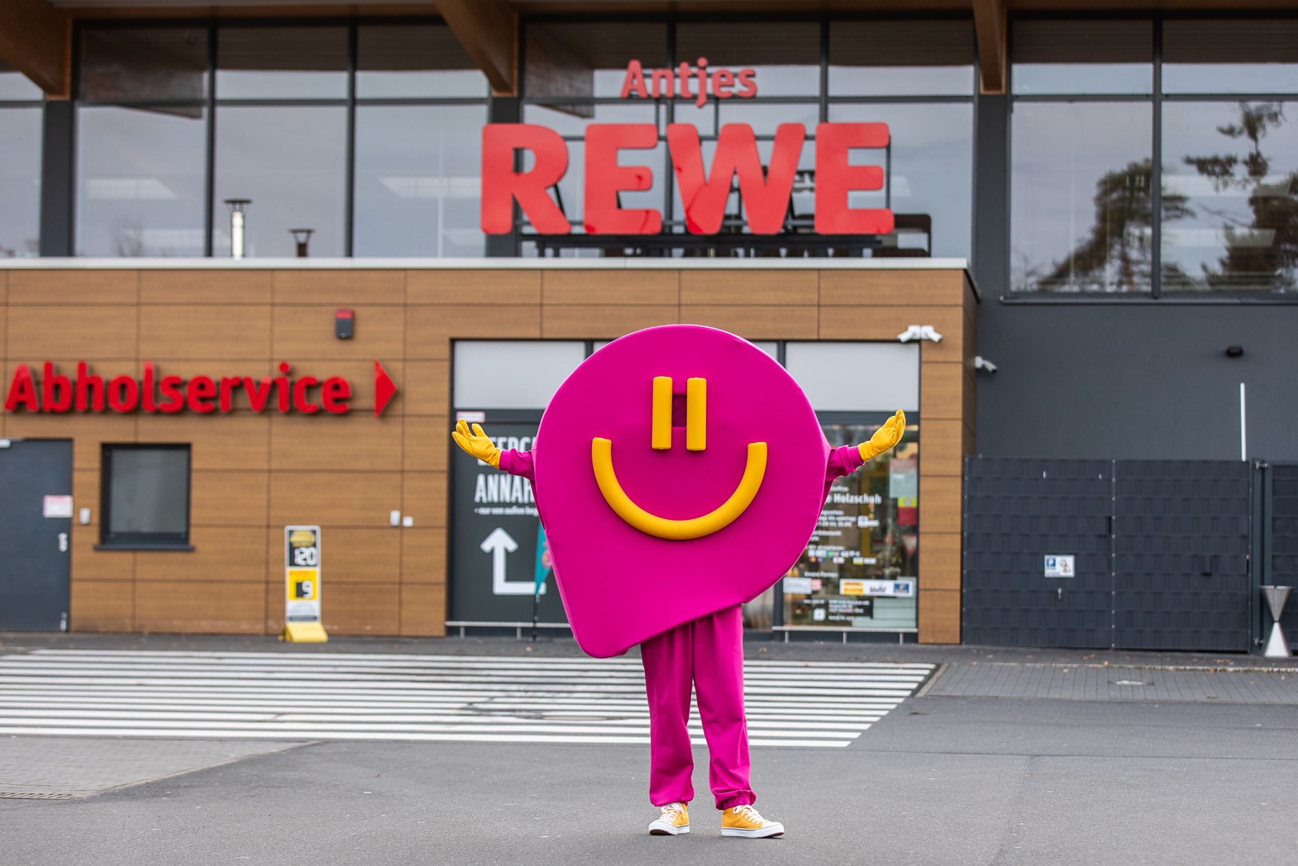 REWE Bonus Maskottchen steht vor dem REWE Markt