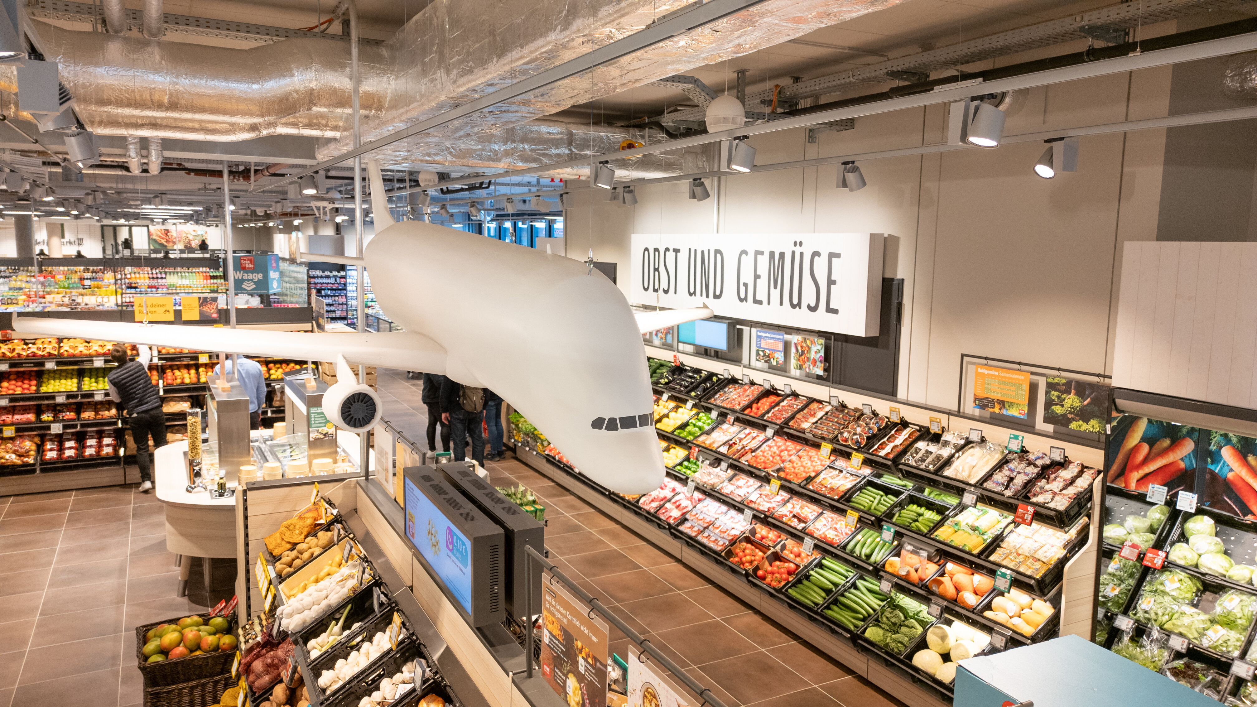 Blick auf die Obst- und Gemüseabteilung mit Flugzeugmodell an der Decke im Fokus.