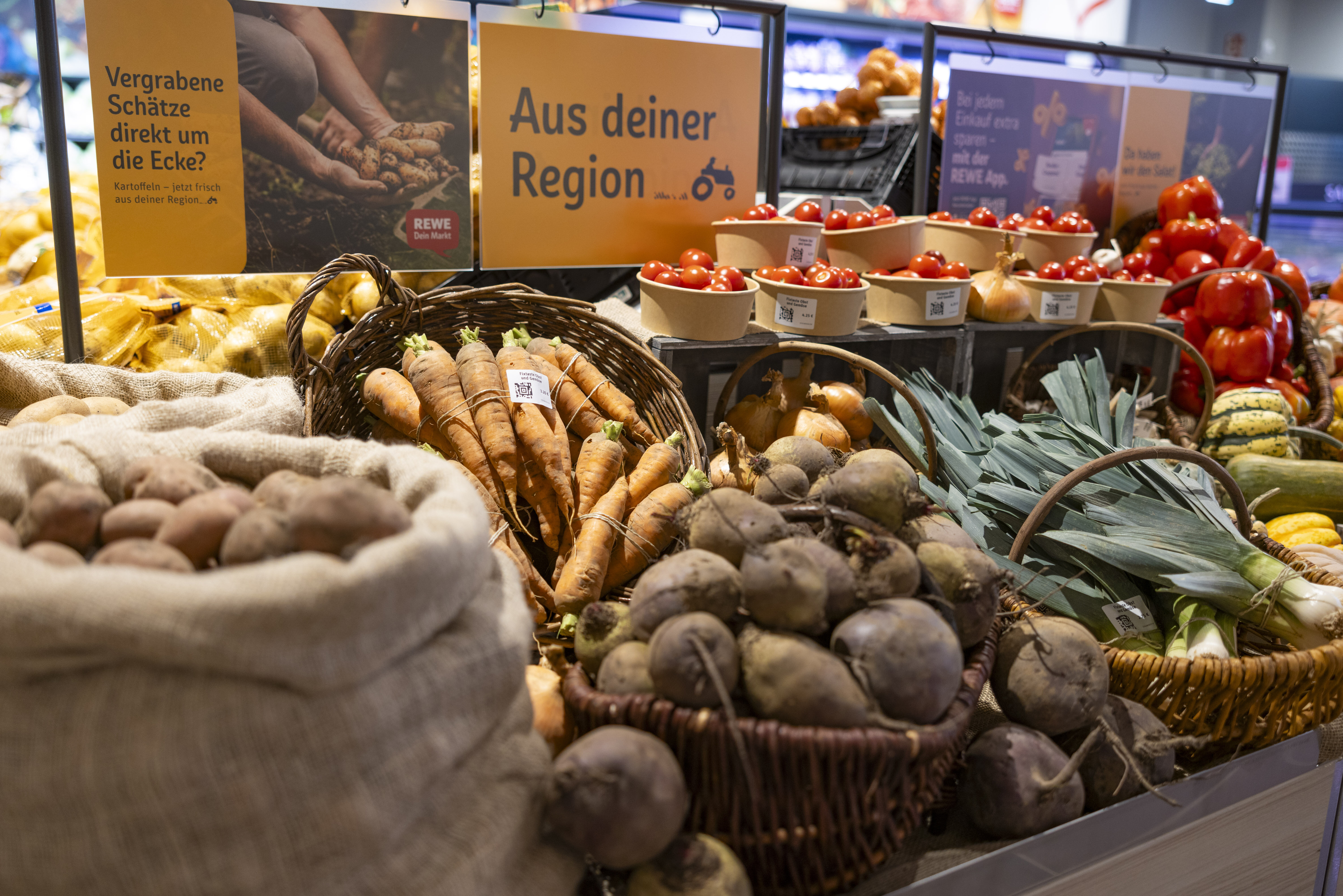Gemüse im Korb (Kartoffeln, Lauch, Karotten) mit Schild "Aus deiner Region" in der Gemüseauslage im REWE-Markt
