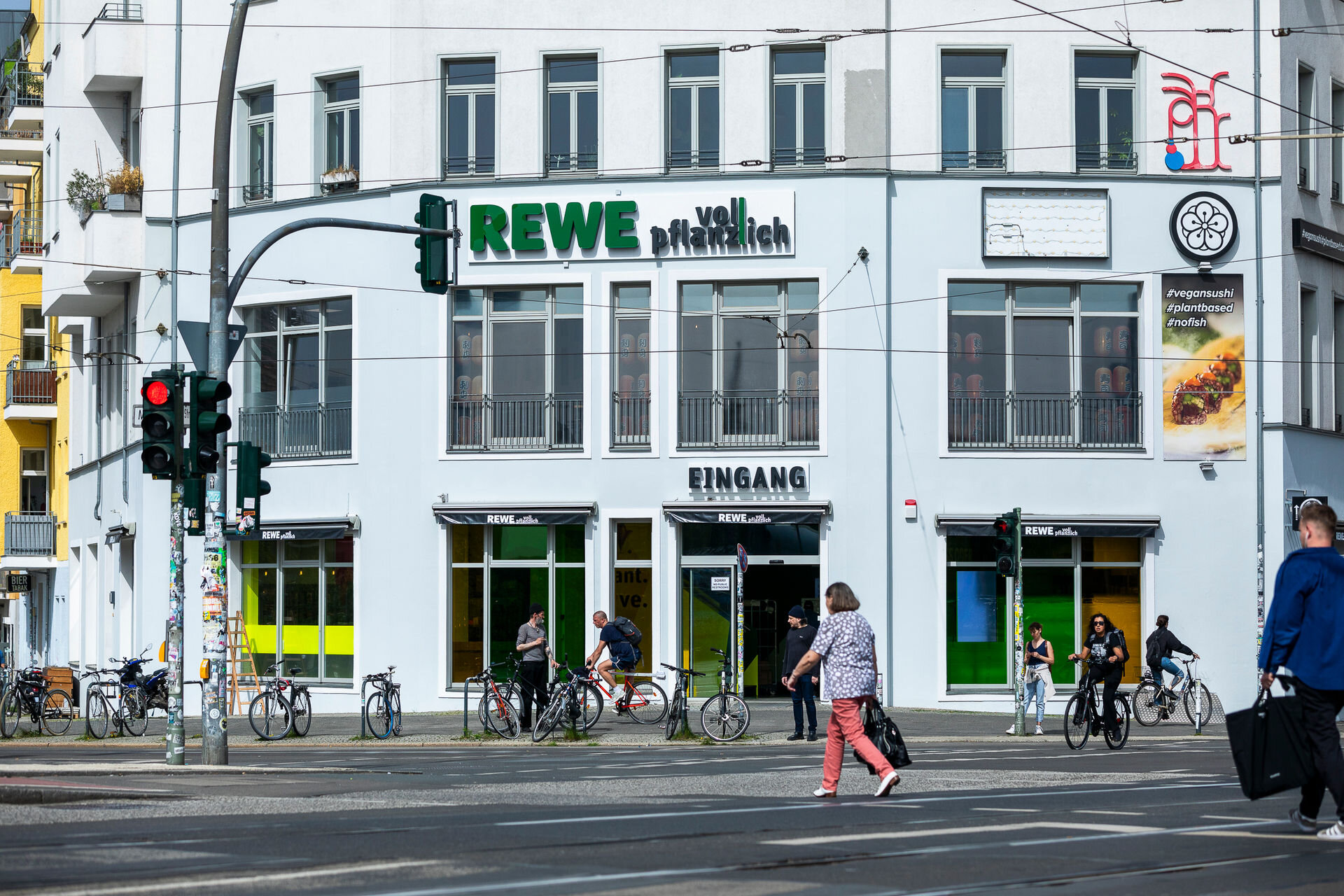 Pflanzlicher Rewe-Markt von außen mit Straße und Radfahrenden davor