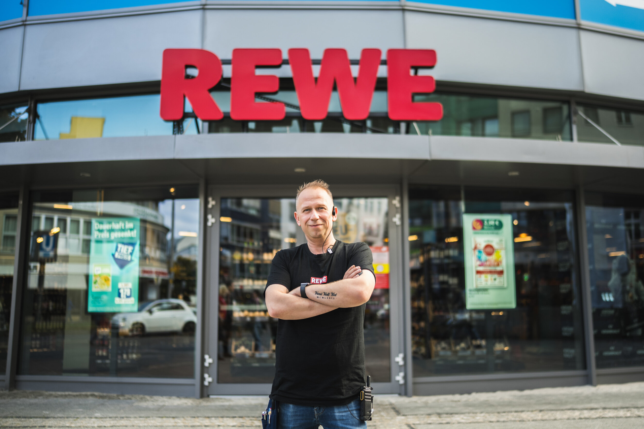 Der REWE-Kaufmann Jirko Lehmberg vor der Glasfasse seines Supermarkts mit verschränkten Armen