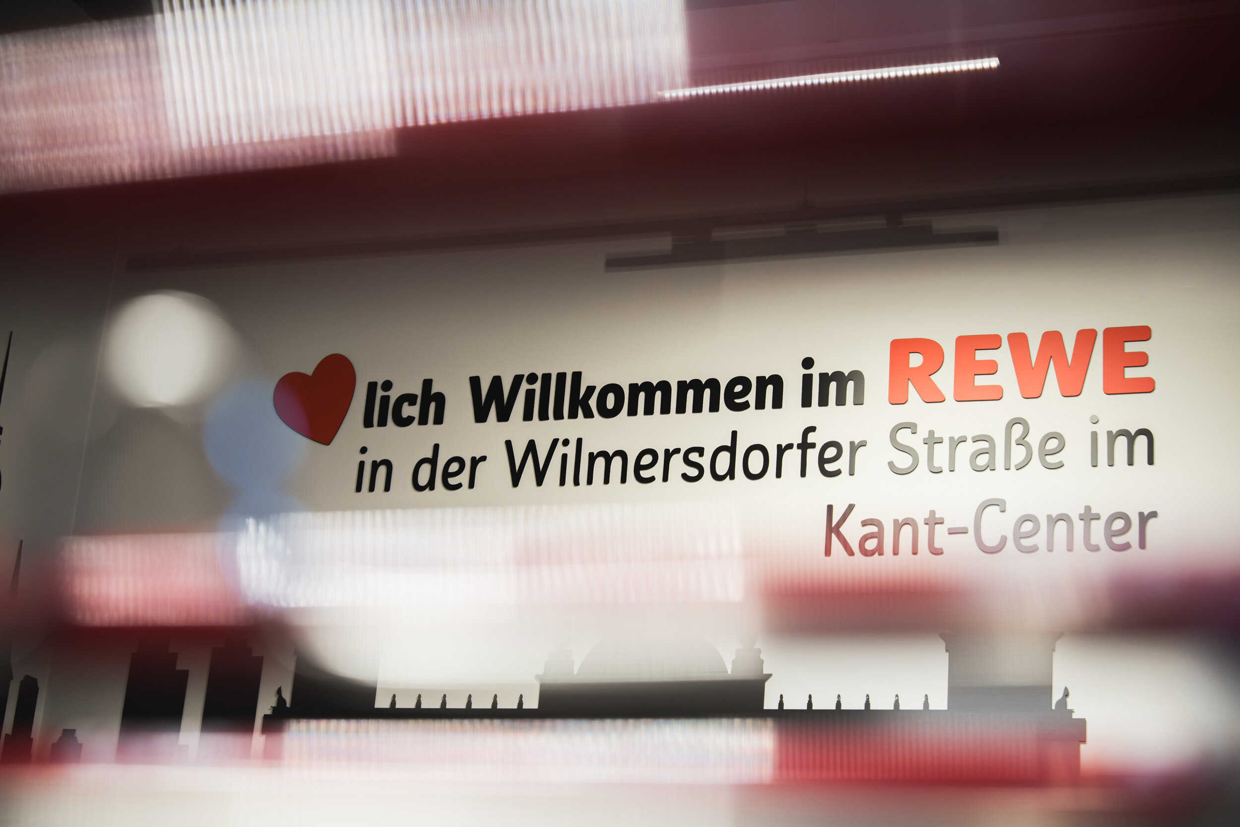 Wanddeko mit Willkommensgruß im REWE im Kant Center mit Einkaufswagen im Vordergrund, unscharf