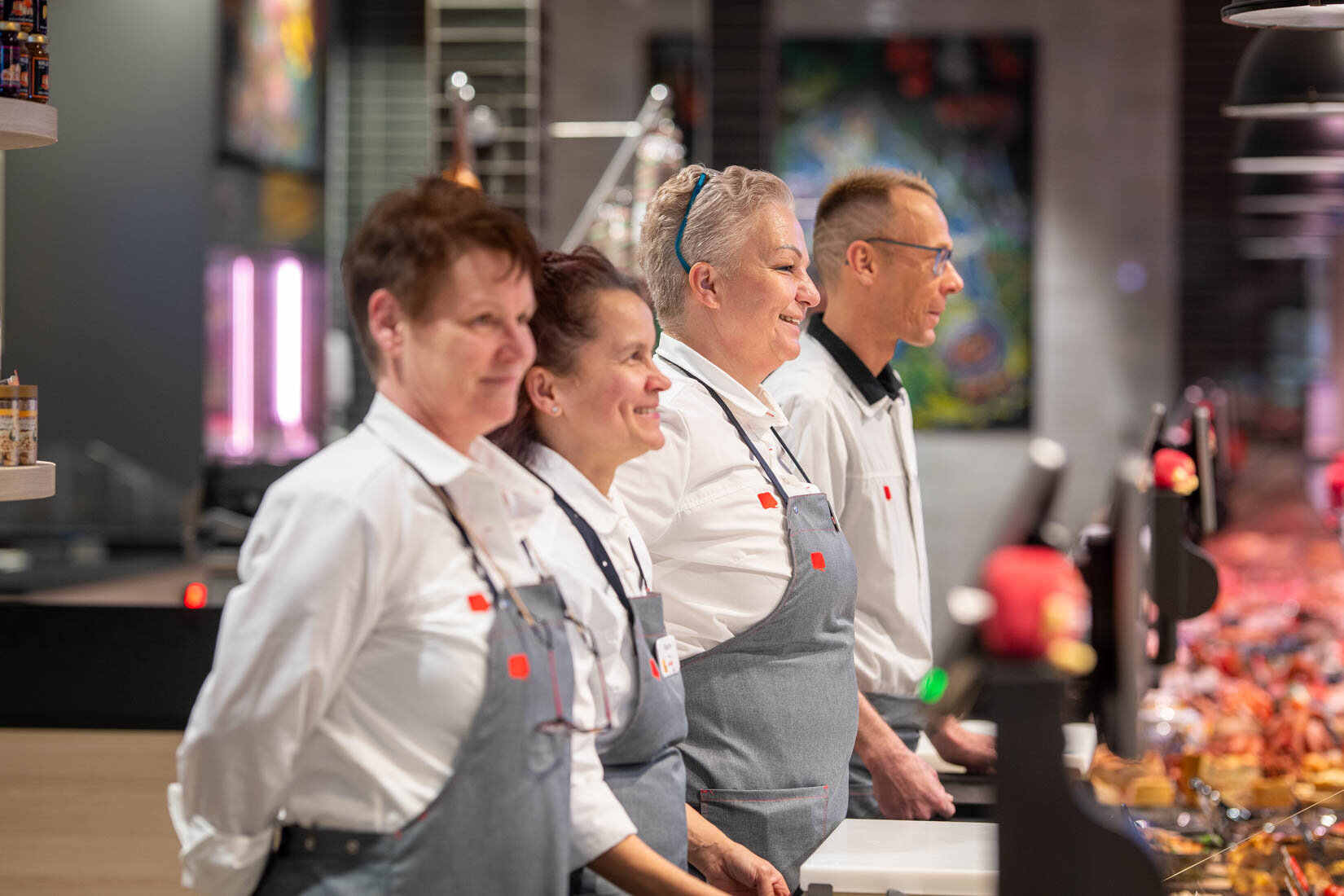 Vier Mitarbeitende in Arbeitskleidung stehen hinter der Bedientheke und lächeln.