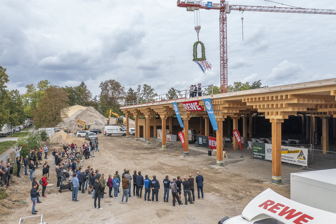 Menschenmenge steht vor einem Gebäude und sieht zu beim Aufsetzen der Richtkrone auf ein Gebäude, das im Bau befindlich ist. Die Aufnahme ist in der Vogelperspektive.