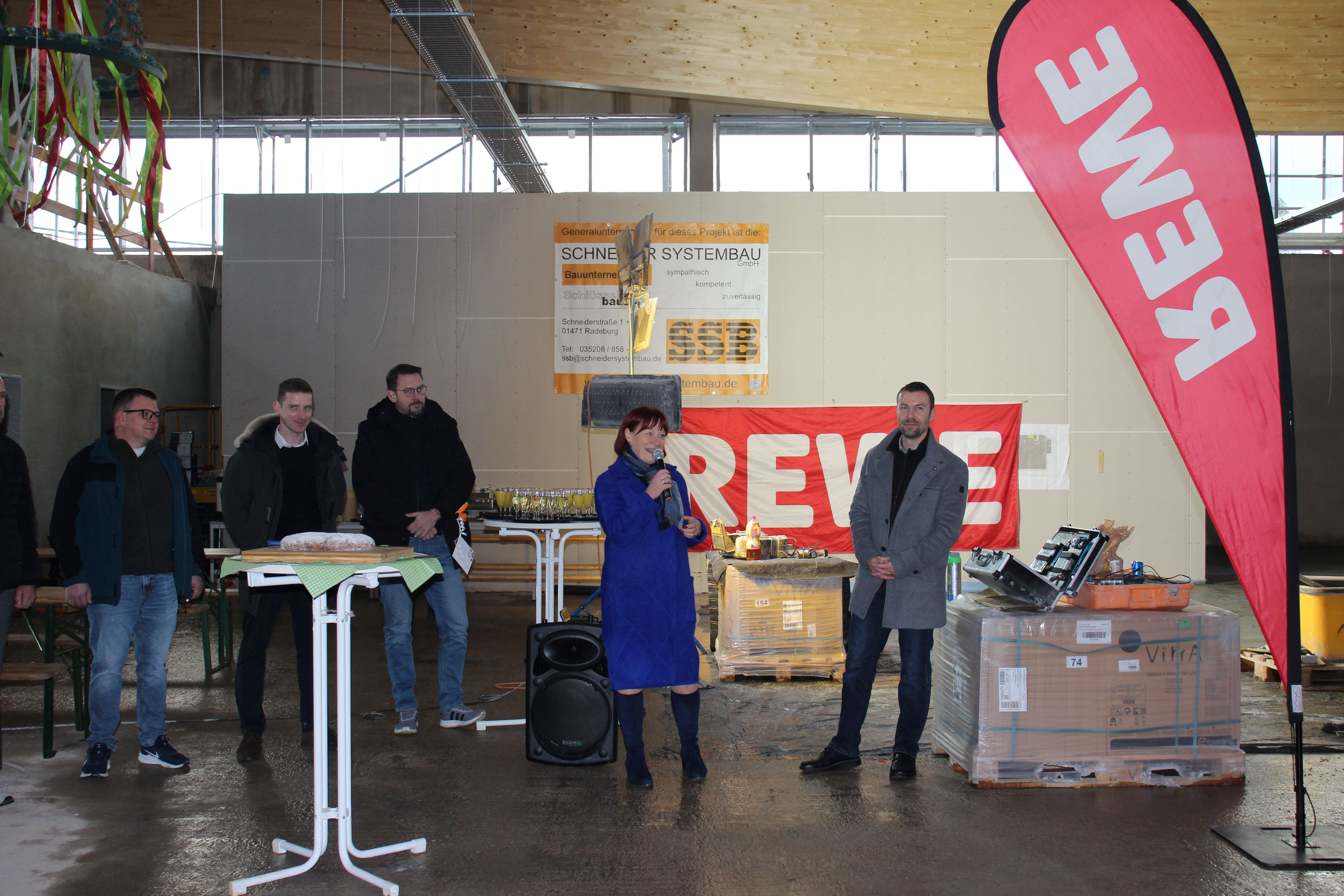 Oberbürgermeisterin Kerstin Körner hält eine Rede. Neben ihr stehen Michael Wolf (REWE-Kaufmann), Jonathan Lennartz (Projektleiter Eigenobjekte Expansion, REWE Ost), Florian Nain (Teamleiter Planung & Eigenobjekte Bauwesen, REWE Ost) und Roman Seifert (Vorstand Bäckerei Bärenhecke)