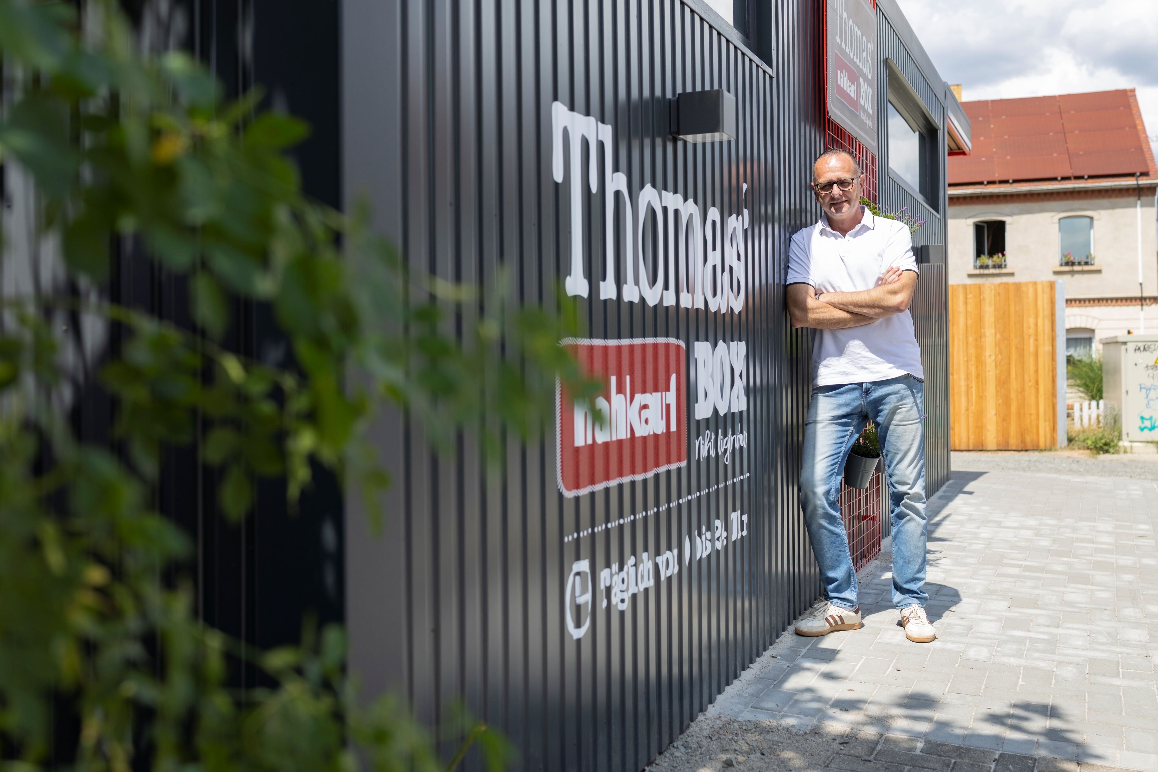 Ein Mann lehnt an einem Container mit der Aufschrift Thomas' nahkauf Box
