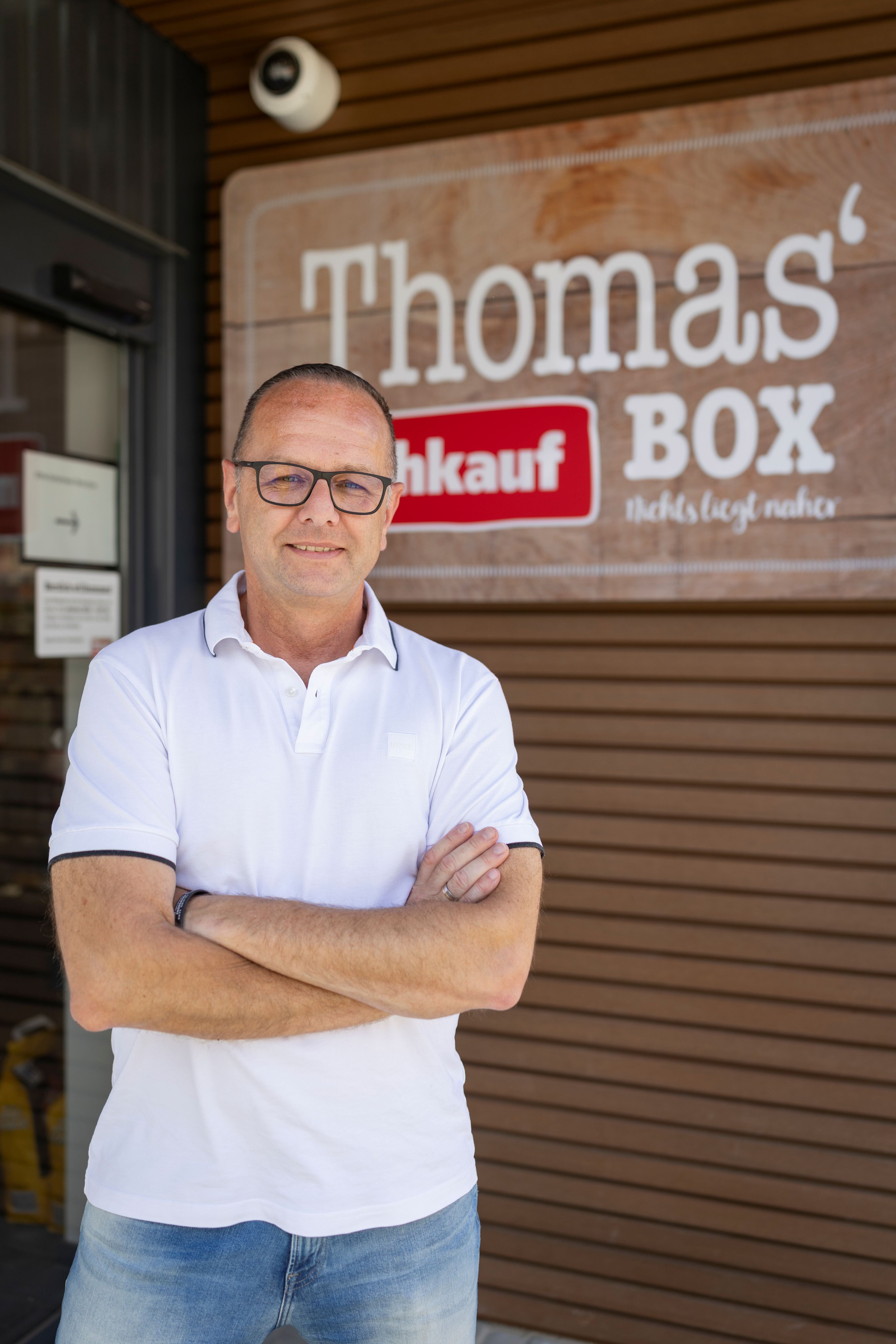 Ein Mann steht mit verschränkten Armen vor der nahkauf Box