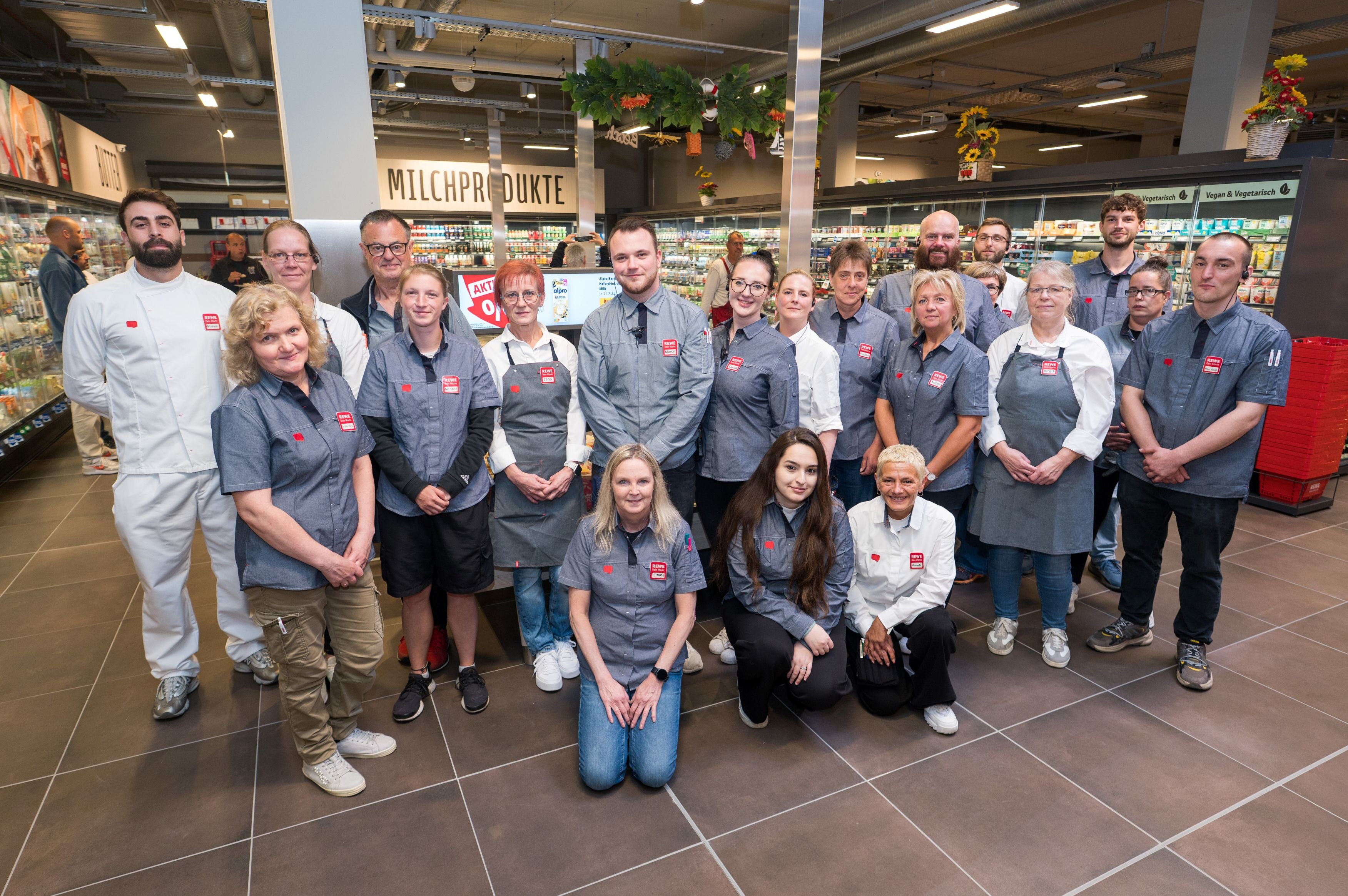 Eine Gruppe an Menschen steht in der Abteilung Molkereiprodukte und schaut in die Kamera
