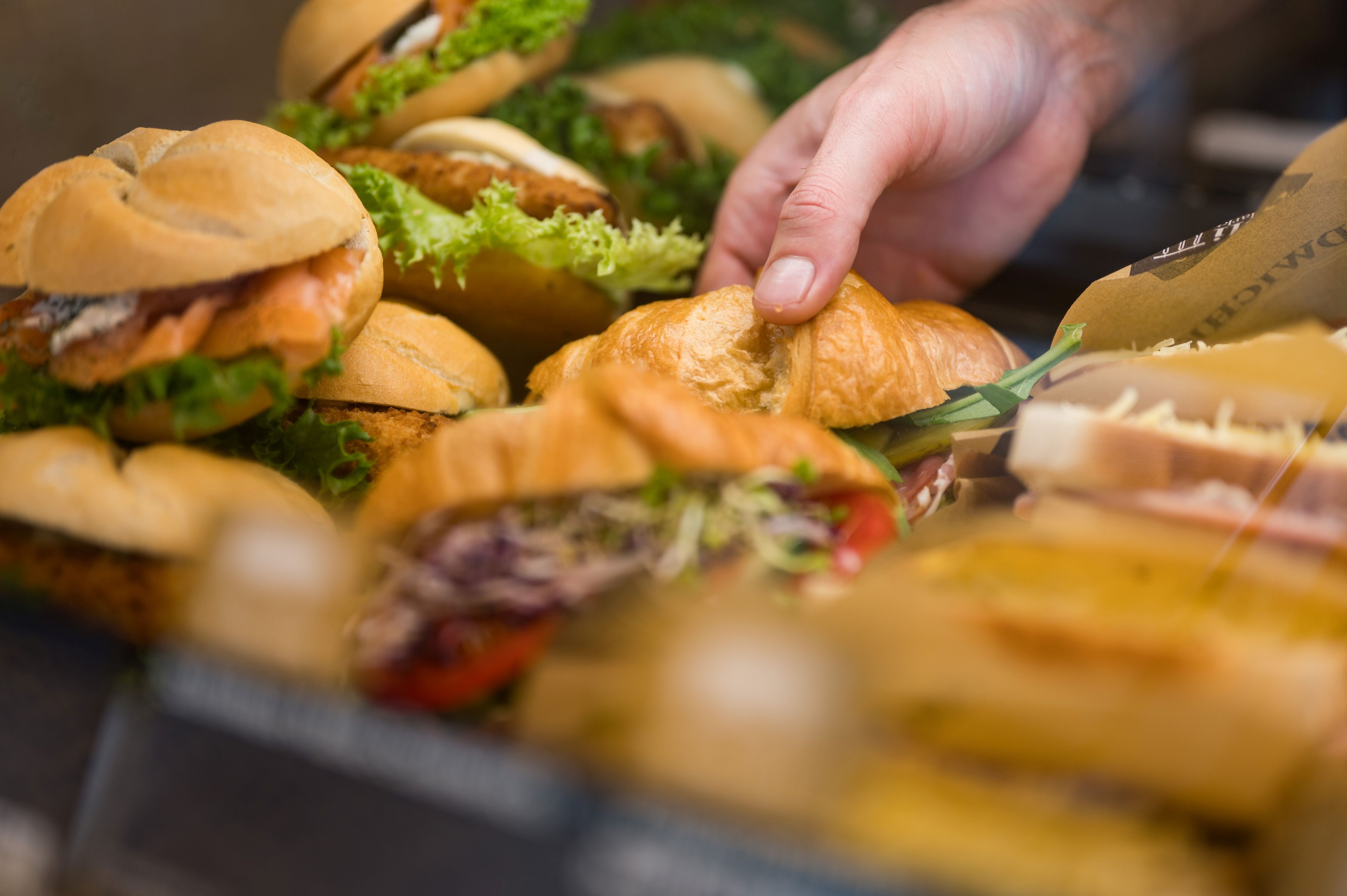 Eine Hand legt ein belegtes Brötchen in eine Auslage