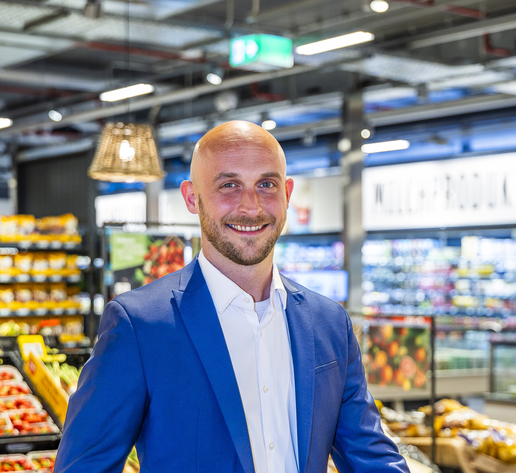 Ein Mann steht in der Obst- und Gemüseabteilung und lächelt in die Kamera. 