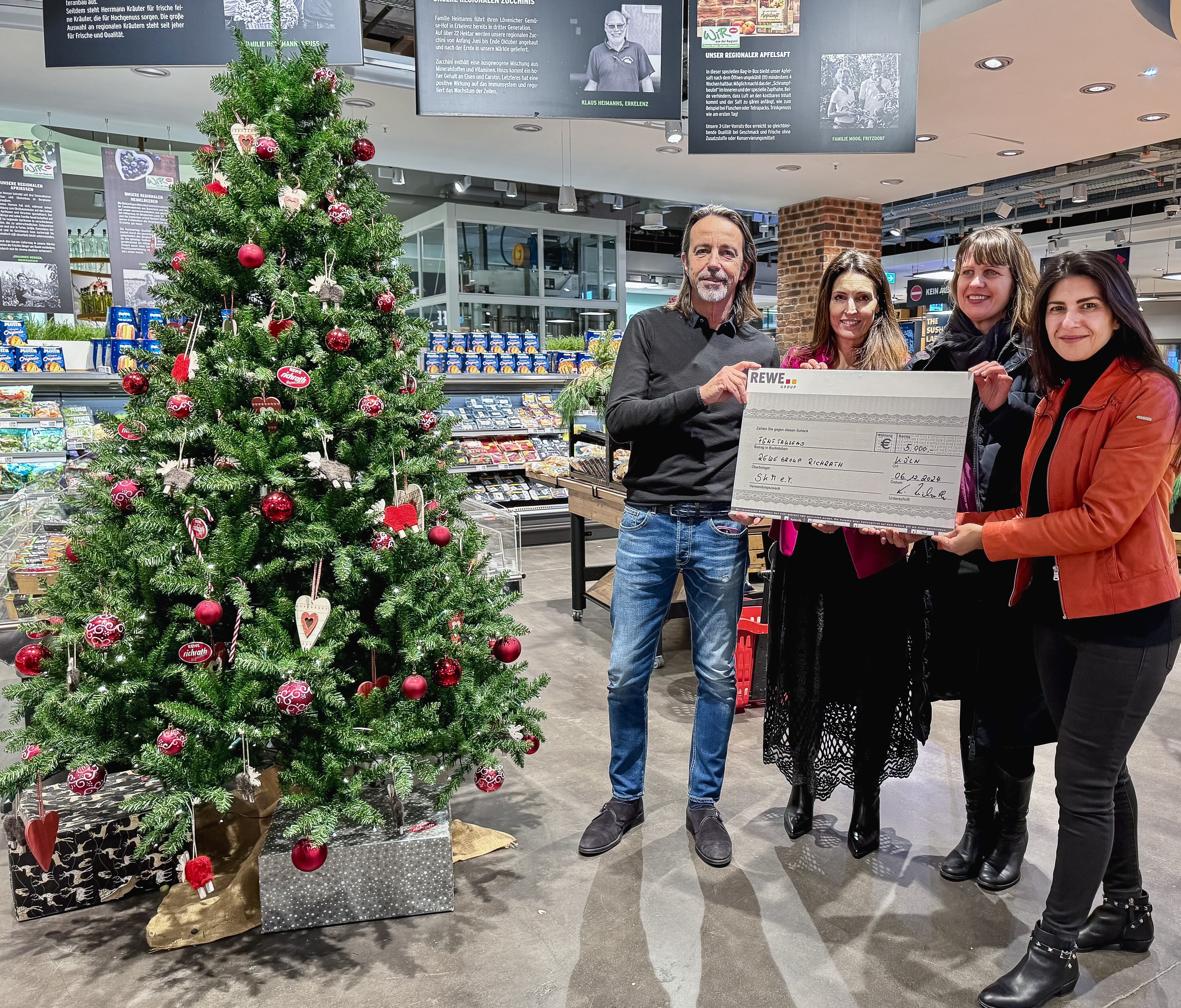 Vier Menschen halten Spendencheck neben Weihnachtsbaum